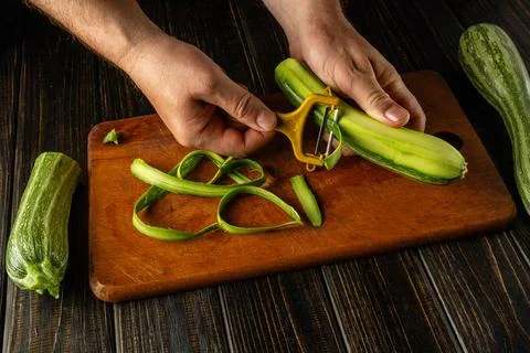 A person is peeling a zucchini using a vegetable peeler while other zucchin.. Stock Photos