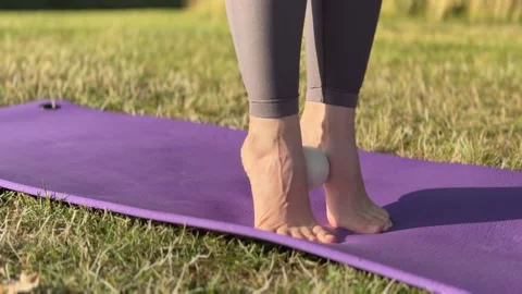 A person performing foot massage using a ball on a yoga mat outdoors. 스톡 동영상 341877567
