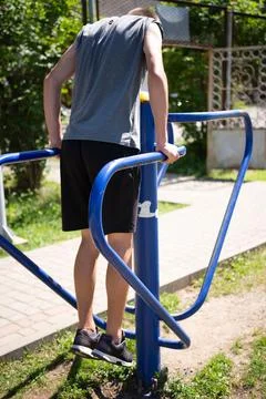 A person performs dips on blue parallel bars at an outdoor gym. The individua Stock Photos