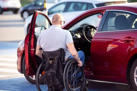Person with a physical disability getting in red car fom wheelchair Foto stock