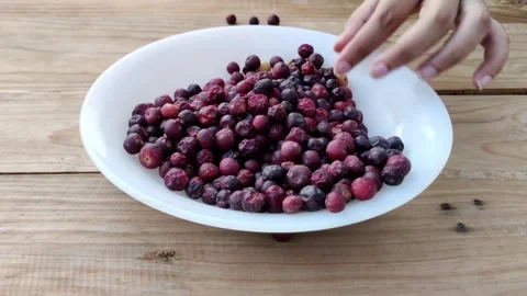 Person picking fallen falsa berries off wood surface putting in bowl Stock Footage 336842241