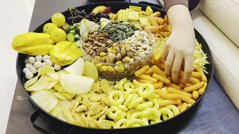 Person picking up snacks from a large circular tray on a desk Stock Footage 345146506
