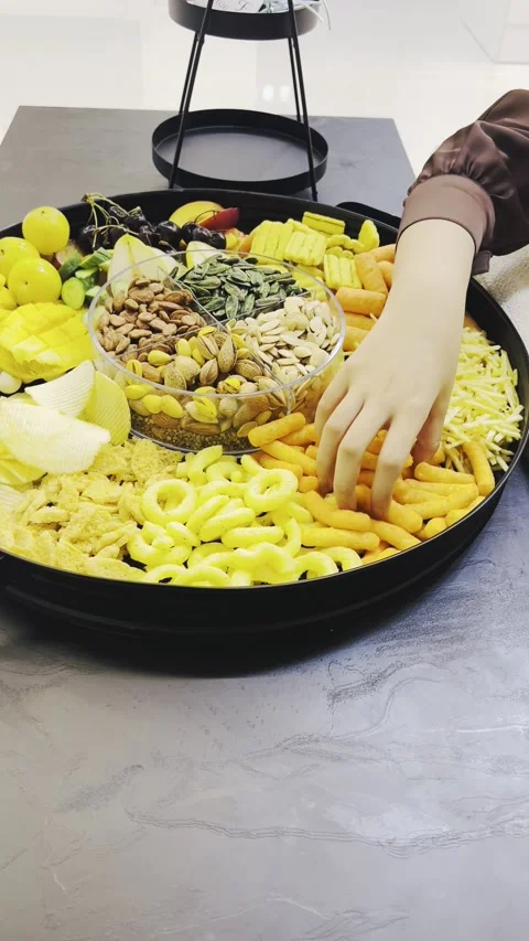 Person picking up snacks from a large circular tray on a desk Stock Footage 345146511