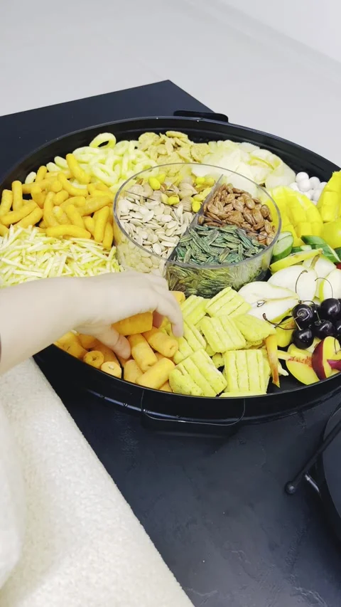 Person picking up snacks from a large circular tray on a desk Stock Footage 345146650