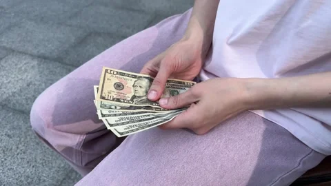 Person in pink pants and white shirt holding and counting US dollar bills  Stockbeeldmateriaal 340261446