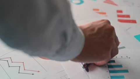 A person places a pen on documents that display various graphs and charts in an Stock-Footage 338302469