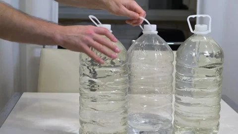 A person places three bottles of drinking water on the kitchen table at home Stock Footage 340209128