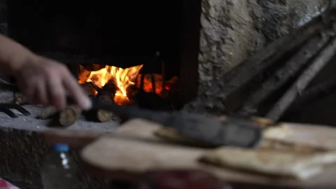 Person placing bread onto baking surface in traditional oven with flames Stock Footage 327324646