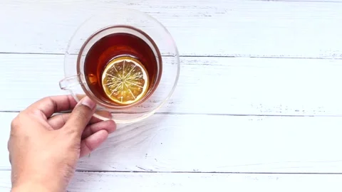 Person placing hot lemon tea glass on white wooden table for a refreshing b.. Stock Footage 332786129