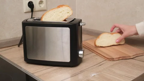 Person placing a slice of bread into a stainless steel toaster on a wooden Stock Footage 293232789