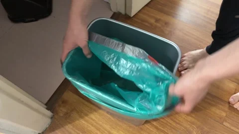 Person placing trash bag into bin in kitchen, waste management routine, home Stock Footage 337109658