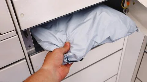 A person is placing a white package into a secure locker for delivery or pickup. Stock Photos