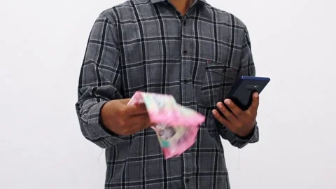 Person In Plaid Shirt Using Mobile Device And Holding Money Against Plain B.. Stock Footage 307051917