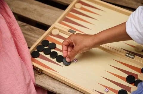 Person playing backgammon with black pieces on a wooden board outdoors Stock Photos