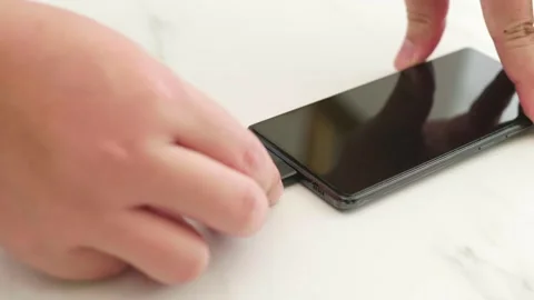 Person plugging charging cable into smartphone on white desk surface. Stock Footage 337402578
