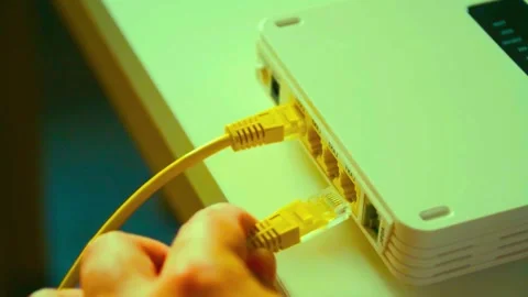 Person plugging a yellow ethernet cable into a wireless internet router Stock Footage 340356955