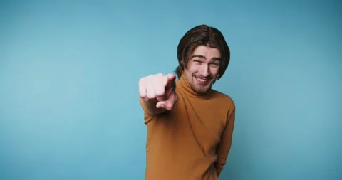 Person pointing and smiling in studio setting with blue background Vídeos de archivo 328249959