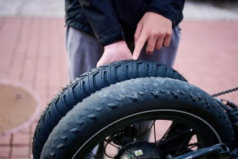 A person is pointing at a bicycle tire while holding it in a city setting. Th Stock Photos