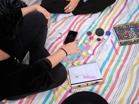 Person pointing to paint samples next to two notebooks on a striped blanket Stock Photos