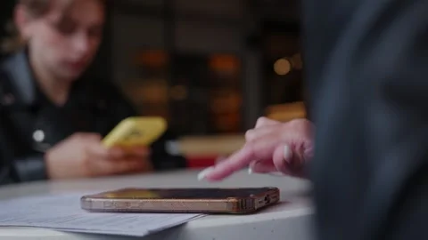 Person pointing at smartphone on table while friend holds yellow phone nearby Stock Footage 339488997
