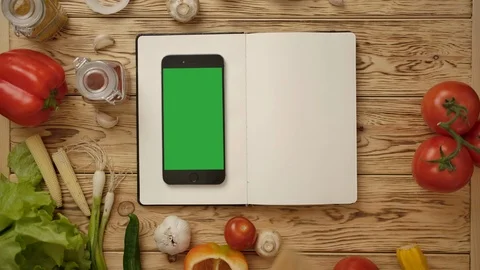 Person pointing with spatula into empty cookbook at table with smartphone Stock Footage 121484643