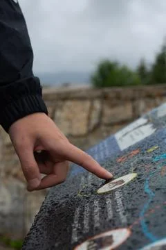 Person points at map on wet display outdoors near greenery and rock wall. Stock Photos