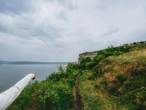 Person points toward a river while standing on a grassy path near a cliff u.. Stock Photos