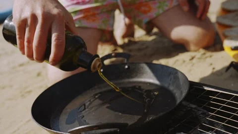 A person is pouring oil into a pan on a beach Stock Footage 298247553