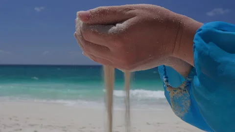 Person pouring sand through hands at tropical beach with ocean waves Stock Footage 346368439