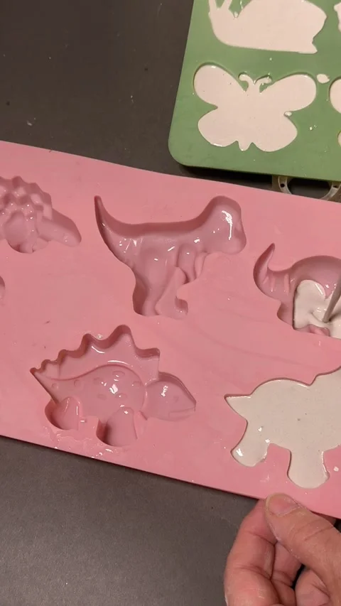 Person pours liquid white plaster into pink silicone mold with dinosaur shapes. Stock Footage 344550494