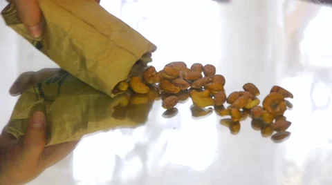 A person pours slowly cashew nuts with paper bag on a mirror table, side view Stock Footage