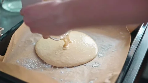 A person pours a thick batter onto a lined baking tray in a kitchen. The action Stock Footage 339096291