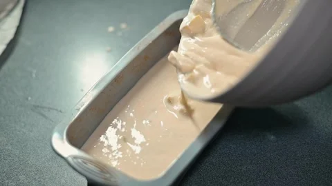 A person pours a thick batter into a loaf pan in a kitchen. The individual is Stock Footage 339097357
