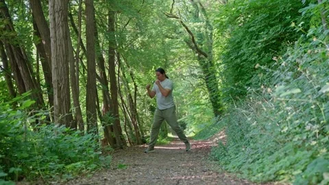 A person practices martial arts techniques while walking along a peaceful wooded Stock Footage 315655680