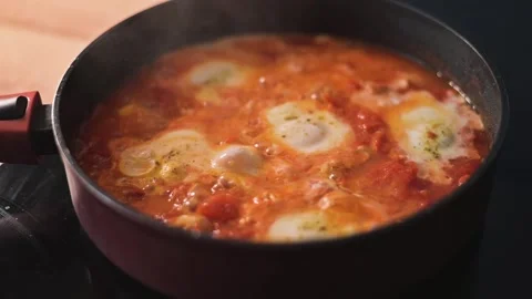 A person prepares a dish in a red pot on the stove, adding eggs to a mixture of Vidéo 344667588