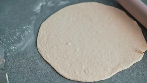 A person prepares dough on a flat surface using a rolling pin. The hands are Stock Footage 339094464