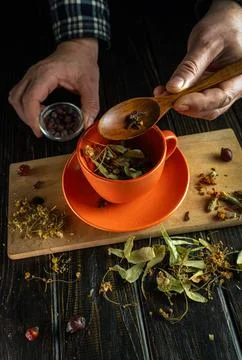A person prepares herbal tea by adding dried leaves and flowers to an orange  Stock Photos