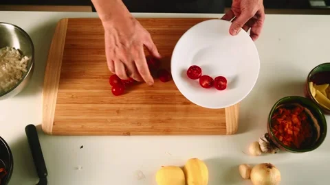 A person prepares ingredients in a spacious kitchen, chopping fresh tomatoes on Video stock 316636104