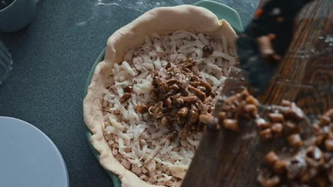 A person prepares a pie crust by adding a layer of shredded ingredients in a Stock Footage 339094553