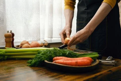 Person prepares vegetables in a kitchen during daylight for a meal Stock Photos