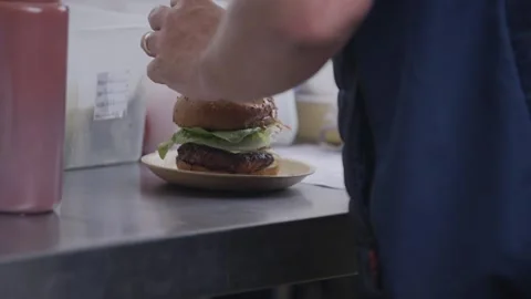 A person is preparing a hamburger with a bun and a bun on a plate Stock Footage 301629933