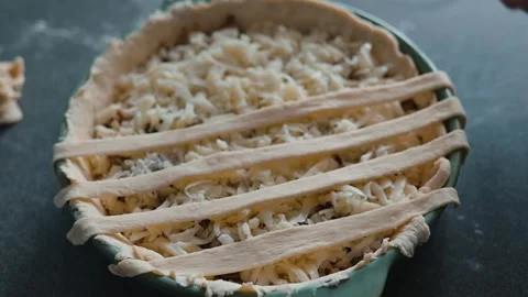 A person is preparing a pie crust by laying strips of dough on top of a filled Video stock 339094614
