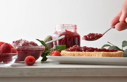 Person preparing toast with raspberry jam on white plate Stock Photos