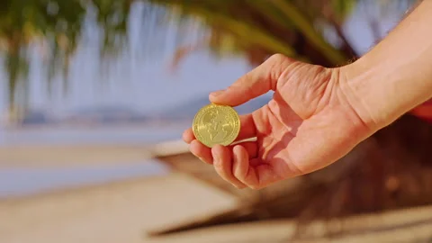 A Person Presents a Gold Tether USDT Token Against a Bright Tropical Shore With Stock Footage 327419491