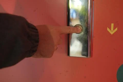 A person presses a button on a silver elevator on an orange wall Foto stock