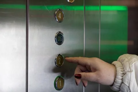 A person presses the elevator button for the second floor inside a modern b.. Stock-Fotos