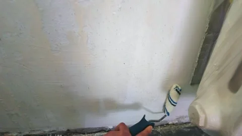 Person priming interior wall with roller near radiator and baseboard Stock Footage 335318106