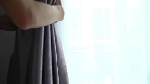 Person pulling back gray curtain to let in sunlight Stock Photos
