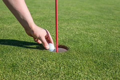 A person pulling a golf ball out of a hole on a golf course golf concept Stock Photos