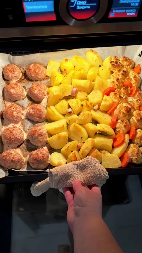 Person pulling hot baking tray with meatballs and roasted potatoes from oven Stock Footage 324534125